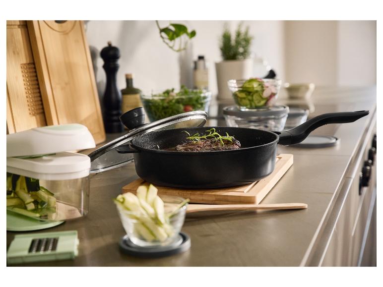 Une poêle noire avec un steak et des herbes, entourée d'ustensiles de cuisine.