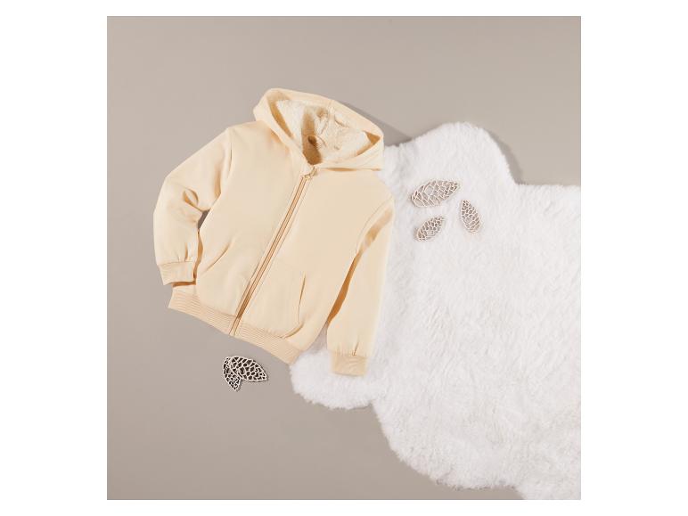 Un sweat à capuche beige avec fermeture éclair sur un tapis en fourrure blanche