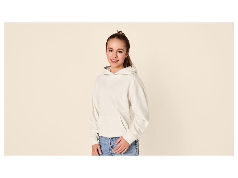 Fille en sweat à capuche beige et jean, souriante.