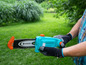 Une personne tenant une tronçonneuse Gardena bleue dans un jardin.
