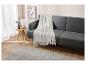 Un plaid blanc moelleux posé sur un canapé gris, dans un intérieur moderne.