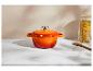 Marmite en fonte orange sur une surface en marbre blanc avec un pot de pâtes et une cuillère en bois.