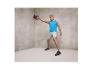 Un homme en débardeur bleu et short gris s'entraîne avec une kettlebell.