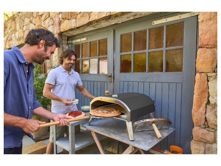 Deux hommes préparent des pizzas en extérieur avec un four à pizza d'extérieur.
