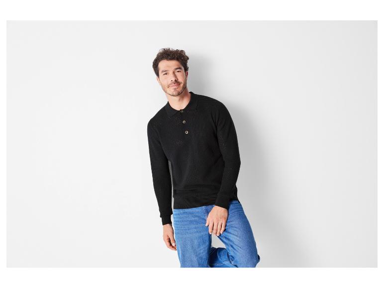 Un homme porte un pull noir à manches longues et un jean bleu.
