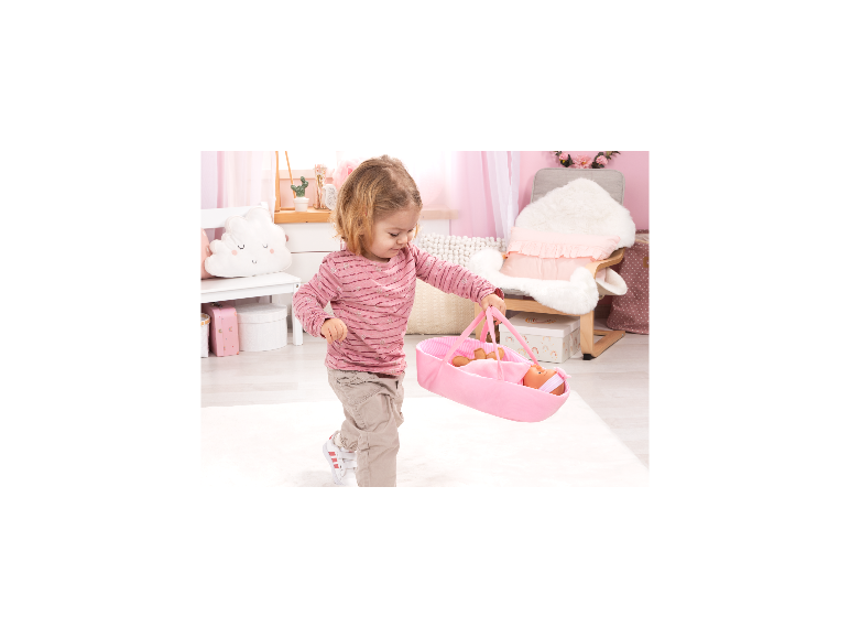 Une petite fille portant un couffin rose de la marque BAYER DESIGN avec un poupon.