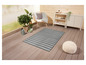 Un tapis d'extérieur rayé sur une terrasse en bois avec une chaise et un pouf.