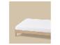 Drap-housse blanc sur un lit en bois clair sur fond beige.