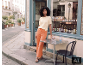 Femme en t-shirt en maille jaune et pantalon large orange devant une boutique.