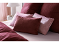 Linge de lit et oreillers dans les tons bordeaux et rose clair, avec rayures et texture velours.