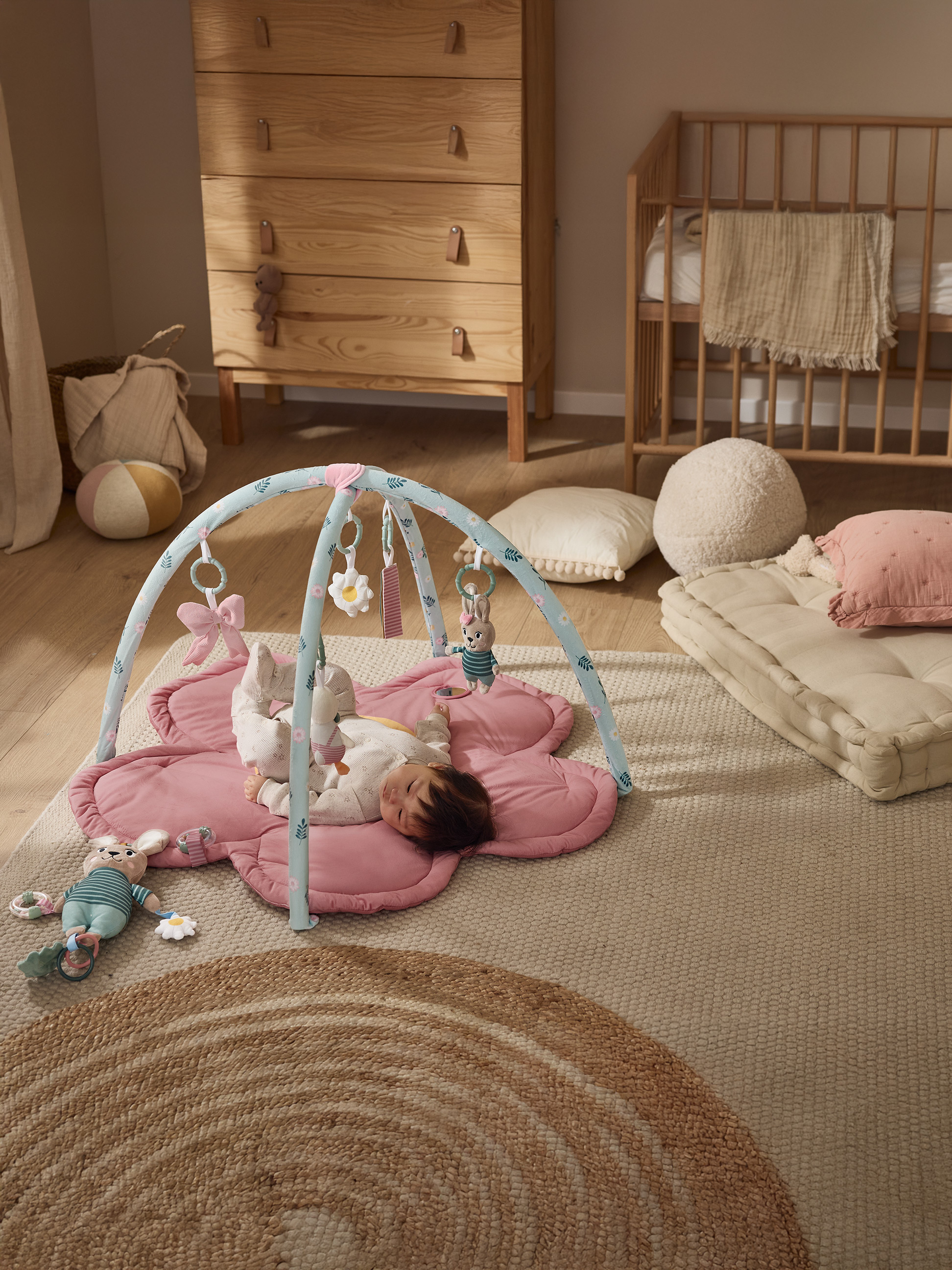 Tapis d'éveil avec arche et jouets, bébé et meubles en bois dans une chambre d'enfant.