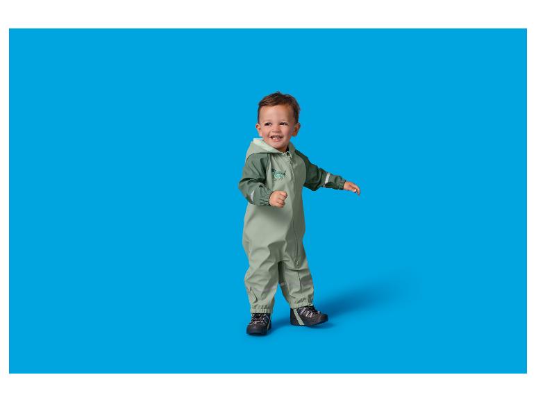 Enfant en bas âge dans une combinaison de pluie verte avec un imprimé dinosaure, souriant et debout.