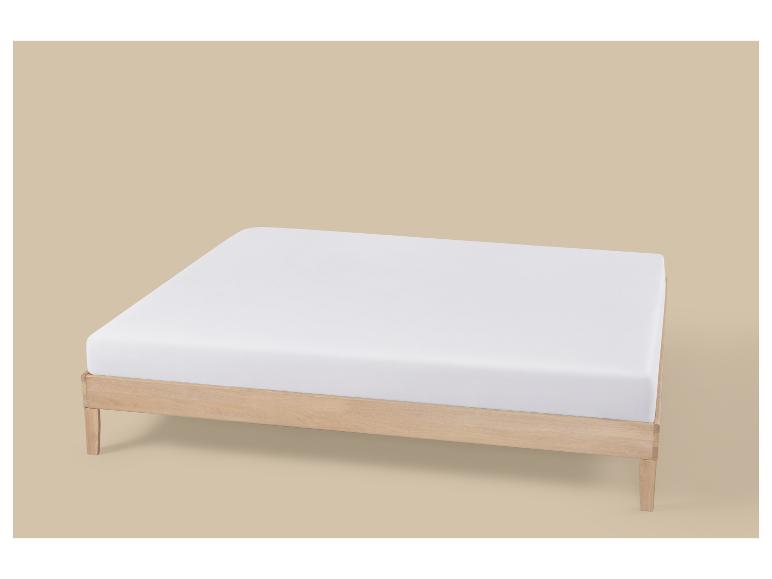 Matelas blanc sur un cadre de lit en bois clair sur fond beige.
