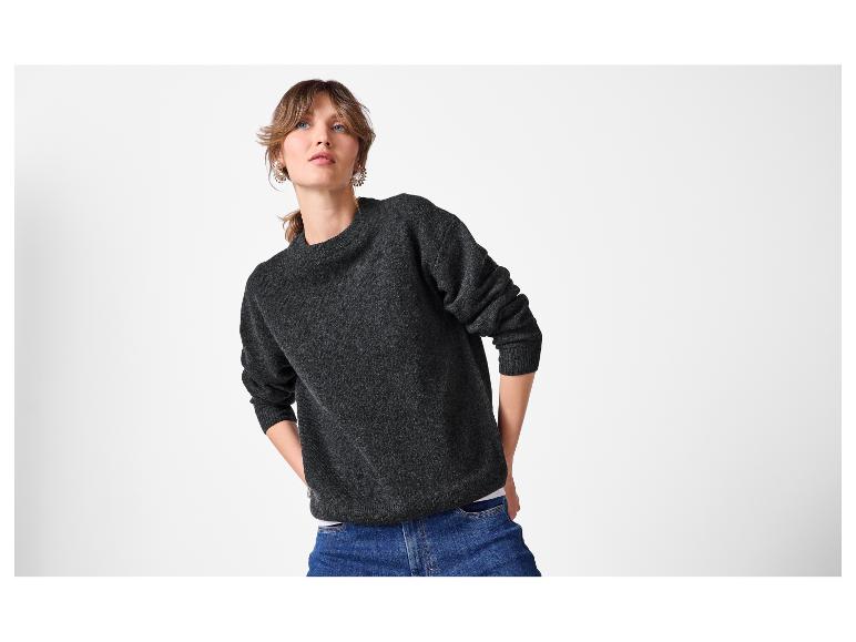 Femme en pull gris foncé et jean bleu, regardant vers le haut.