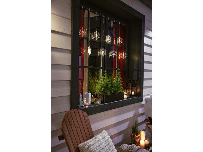 Décoration de fenêtre de Noël avec flocons lumineux, verdure et bougies.