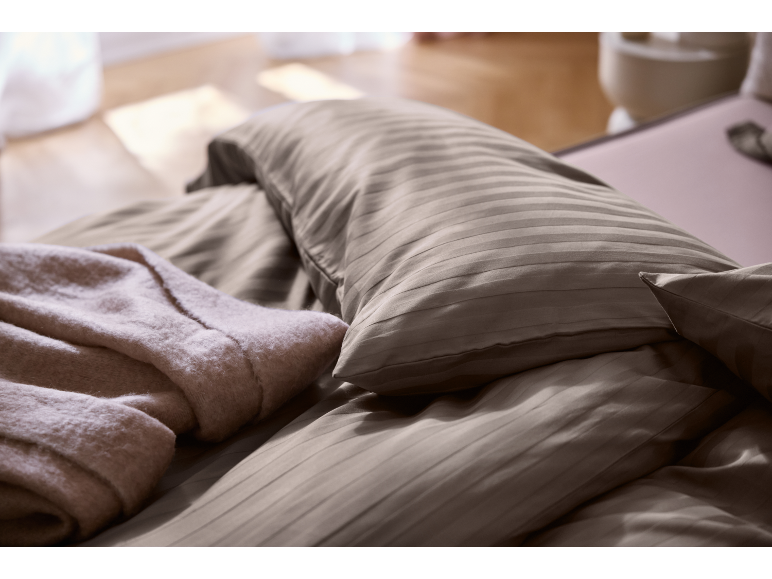 Gros plan d'un lit avec une parure de lit marron rayée et une couverture rose clair.