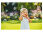 Une petite fille en robe blanche s'amuse avec des bulles de savon dans le jardin.
