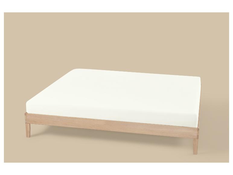 Cadre de lit en bois clair avec matelas blanc sur fond beige.
