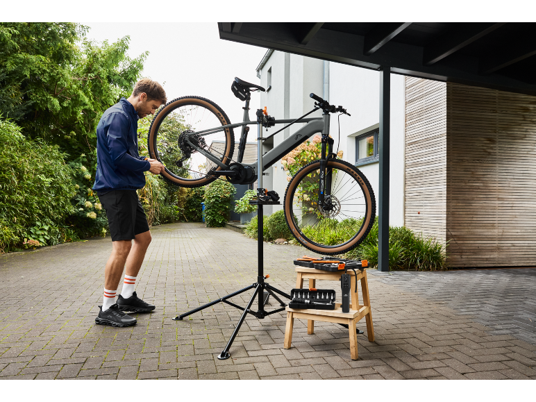 Homme réparant un VTT électrique sur un support de réparation avec des outils à côté.