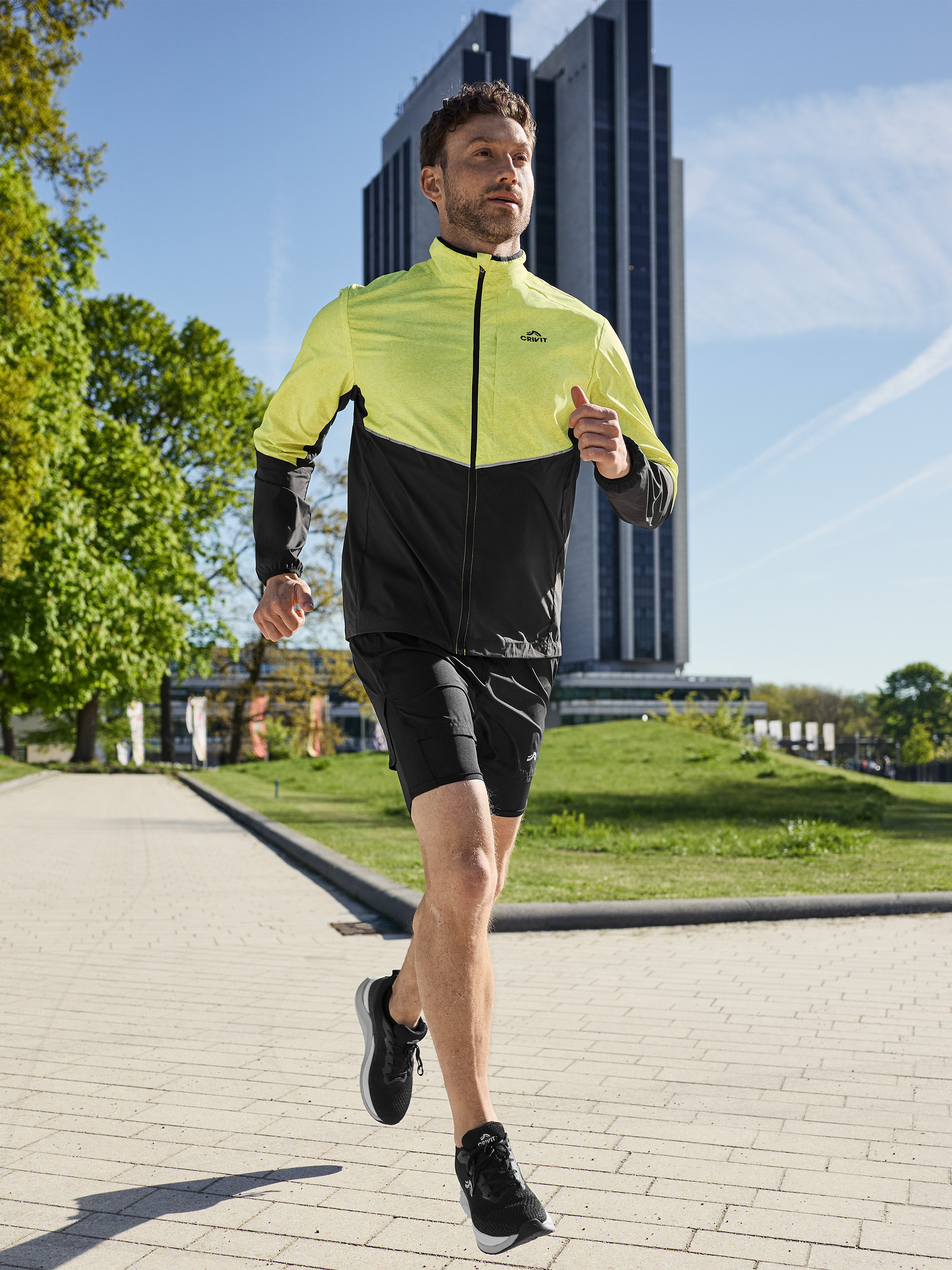 Homme en veste de course jaune et noire et short noir, courant en extérieur.