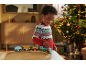 Enfant souriant joue avec un train en bois, sapin de Noël illuminé en arrière-plan.