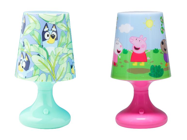 Deux lampes de table pour enfants : une avec des personnages de chiens bleus et des feuilles vertes, l'autre avec des personnages de cochons dans un champ.