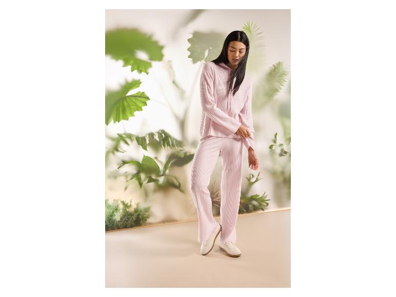 Femme en sweat à capuche côtelé rose et pantalon assorti, entourée de plantes vertes.