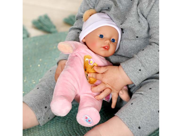 Un enfant tient un poupon vêtu d'un pyjama rose et d'un bonnet blanc.