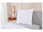 Oreiller et couette blancs matelassés sur un lit gris.