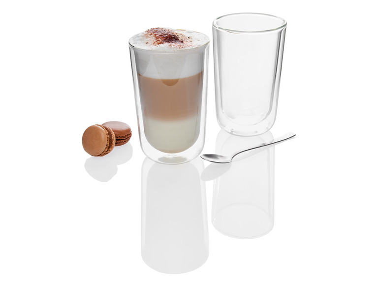 Un latte macchiato dans un verre, deux macarons au chocolat et une cuillère.