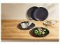 Assiettes noires avec côtelettes d'agneau, légumes et couverts sur une table en bois.