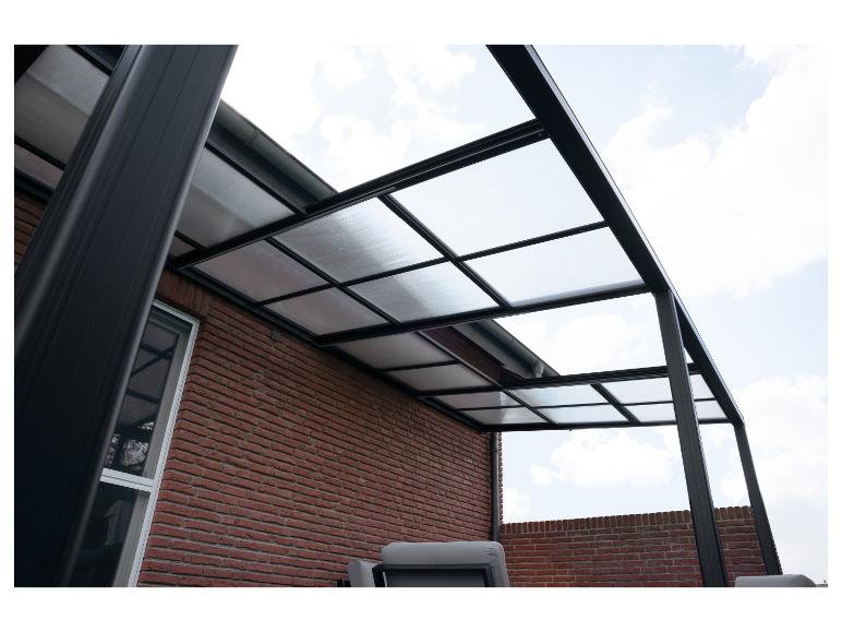 Auvent de terrasse avec toit transparent et cadre noir fixé à un mur de briques.
