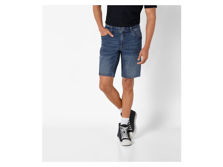 Un homme portant un short en jean bleu foncé et des baskets noires.