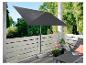Un parasol noir sur un balcon avec une chaise longue et des plantes.