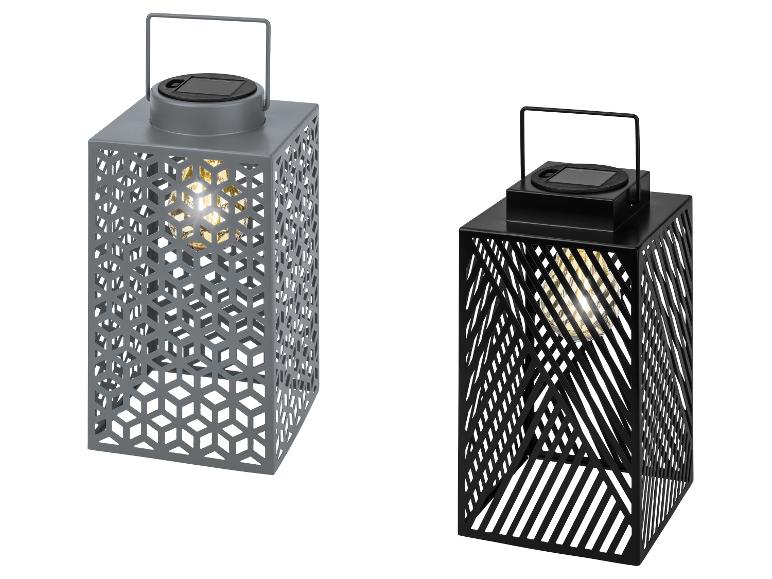 Deux lanternes solaires grises et noires avec des motifs découpés et des ampoules allumées.