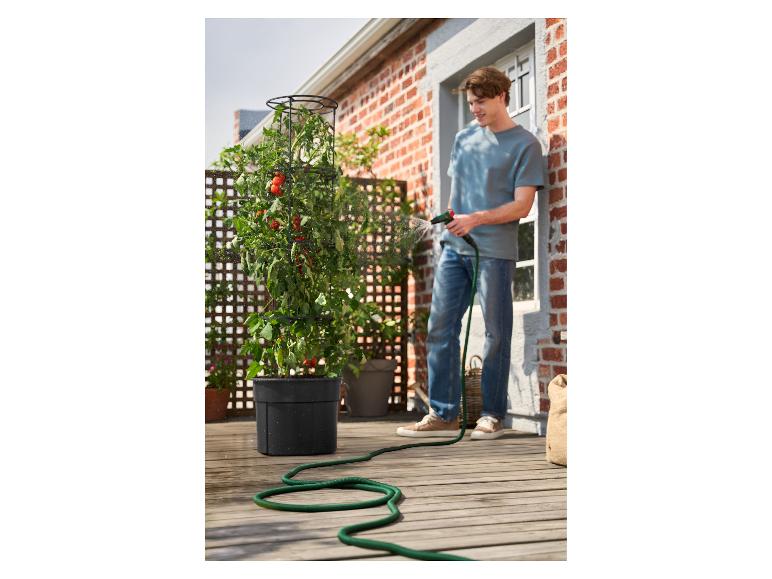 Jeune homme arrosant des tomates cerises dans un pot de fleurs sur un balcon en bois.
