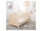 Un lit bébé en bois clair dans une chambre d'enfant avec des œuvres d'art arc-en-ciel et une lampe tissée.