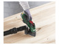 Une ponceuse verte avec aspirateur utilisée sur une surface en bois.