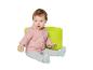 Bébé en sweat à capuche rose et pantalon gris, assis sur un pouf vert avec un bloc en bois.