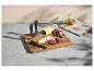 Planche à fromages avec couteaux, fromages, raisins et figues, à côté d'huile d'olive et d'un torchon.