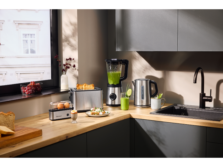 Ensemble de petit-déjeuner de cuisine: grille-pain, mixeur, bouilloire, cuiseur à œufs et aliments frais sur plan de travail en bois.
