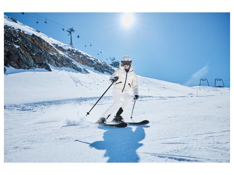 Une femme en veste et pantalon de ski blancs descend une piste.