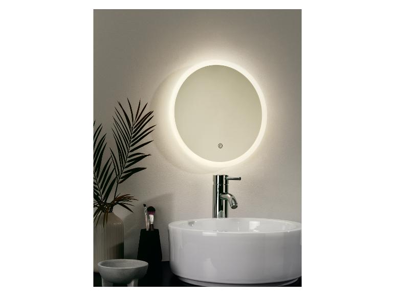 Un miroir rond éclairé au-dessus d'un lavabo dans une salle de bain.
