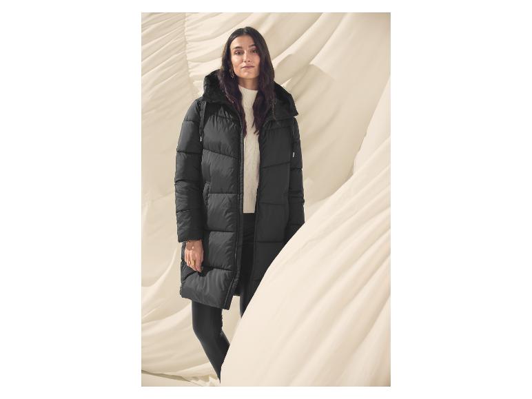 Femme en longue doudoune noire avec un pull blanc, sur fond beige.