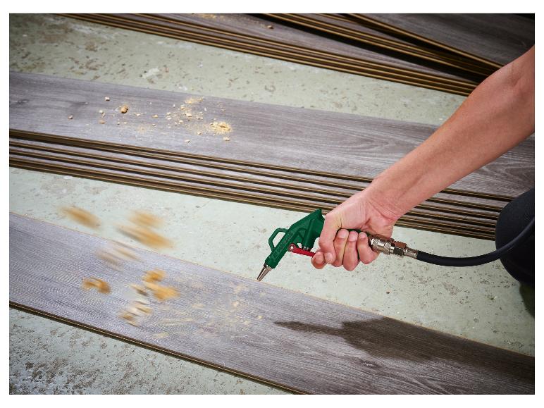 Une personne utilisant un pistolet à air comprimé pour nettoyer la sciure d'une planche de stratifié.