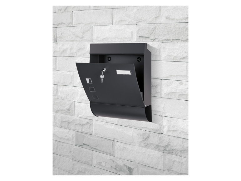 Une boîte aux lettres noire avec une clé visible, fixée à un mur de briques blanches.