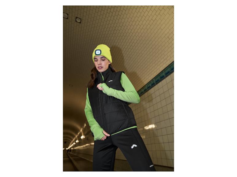 Femme en gilet noir, haut vert et bonnet jaune lumineux dans un tunnel.