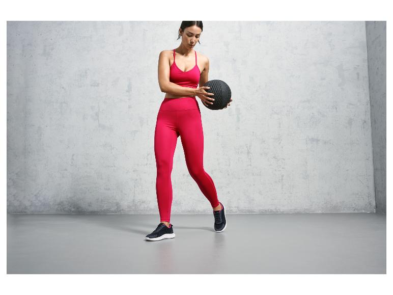 Une femme portant des vêtements de sport roses tenant un ballon de médecine noir.