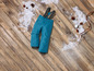 Pantalon de ski bleu avec bretelles sur un sol en bois avec de la neige