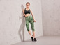 Femme en leggings de sport verts et baskets noires avec une corde à sauter.